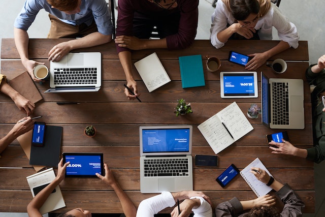 a group of people sitting around a conference table with various tablets and documents